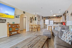 A living room with a sofa, wooden coffee table, and a dining area with chairs and a table. - Main channel view, playground, no steps enrty (Lake Ozark)