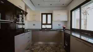 A modern kitchen with a central island, built-in appliances, and a large window providing natural light. - Djerba Villa Piscine Prestige (Temlel)
