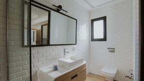 A modern bathroom with white brick walls, a white sink, a wooden vanity, a mirror, and a toilet. - Djerba Villa Piscine Prestige (Temlel)