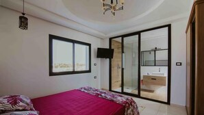 A bedroom with a bed, a TV, a sliding glass door to a bathroom, and a city view. - Djerba Villa Piscine Prestige (Temlel)