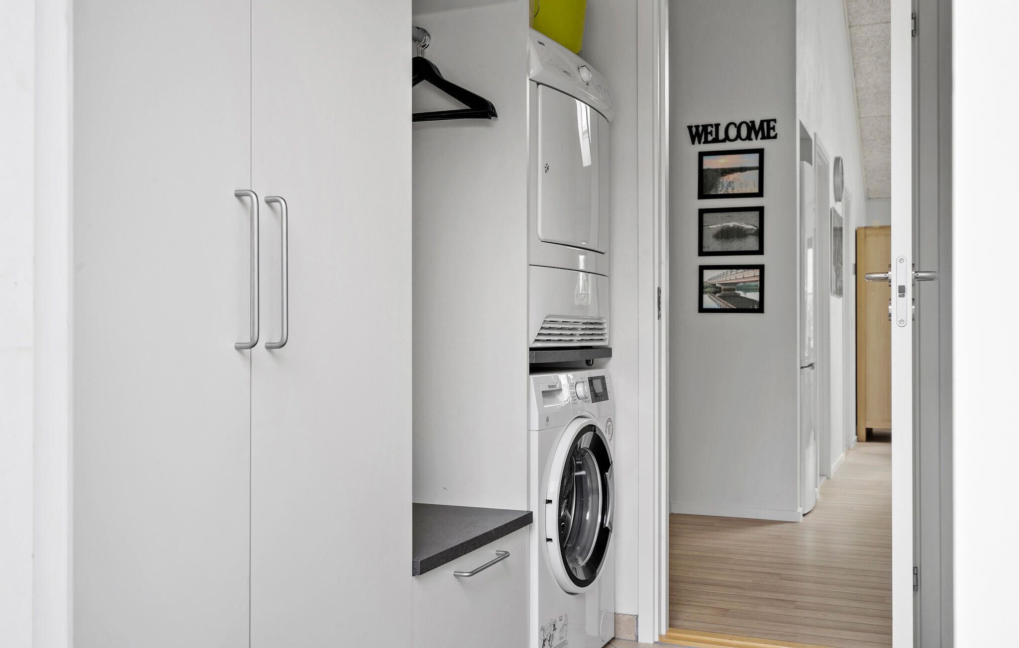 Ein moderner Waschraum mit einer Waschmaschine mit Frontlader, einem Wäscheständer und einem Schild mit der Aufschrift 'WELCOME' und Bildern an der Wand.
