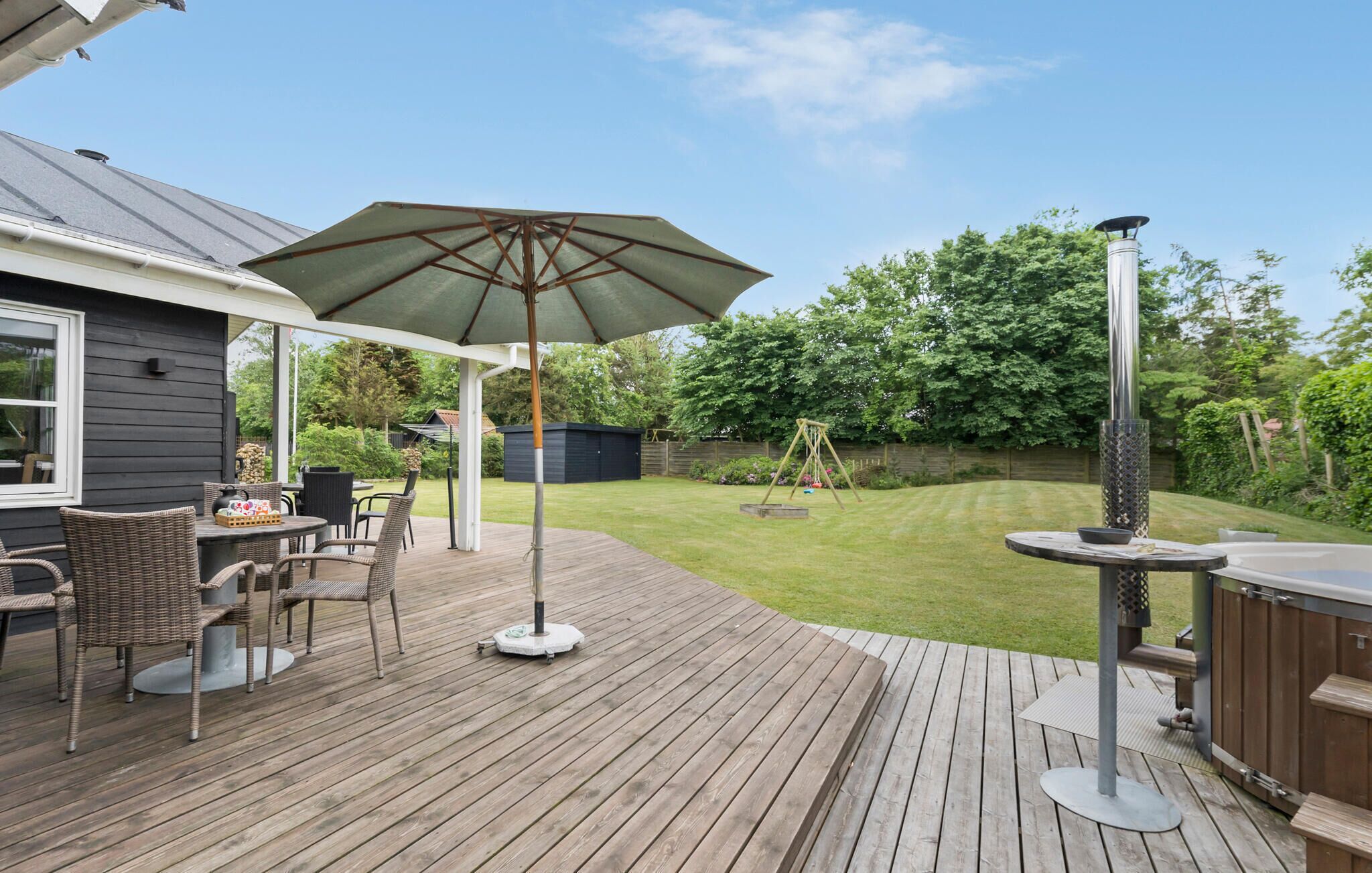 Eine Holzterrasse mit Gartenmöbeln, einer Schaukel und einem Whirlpool.
