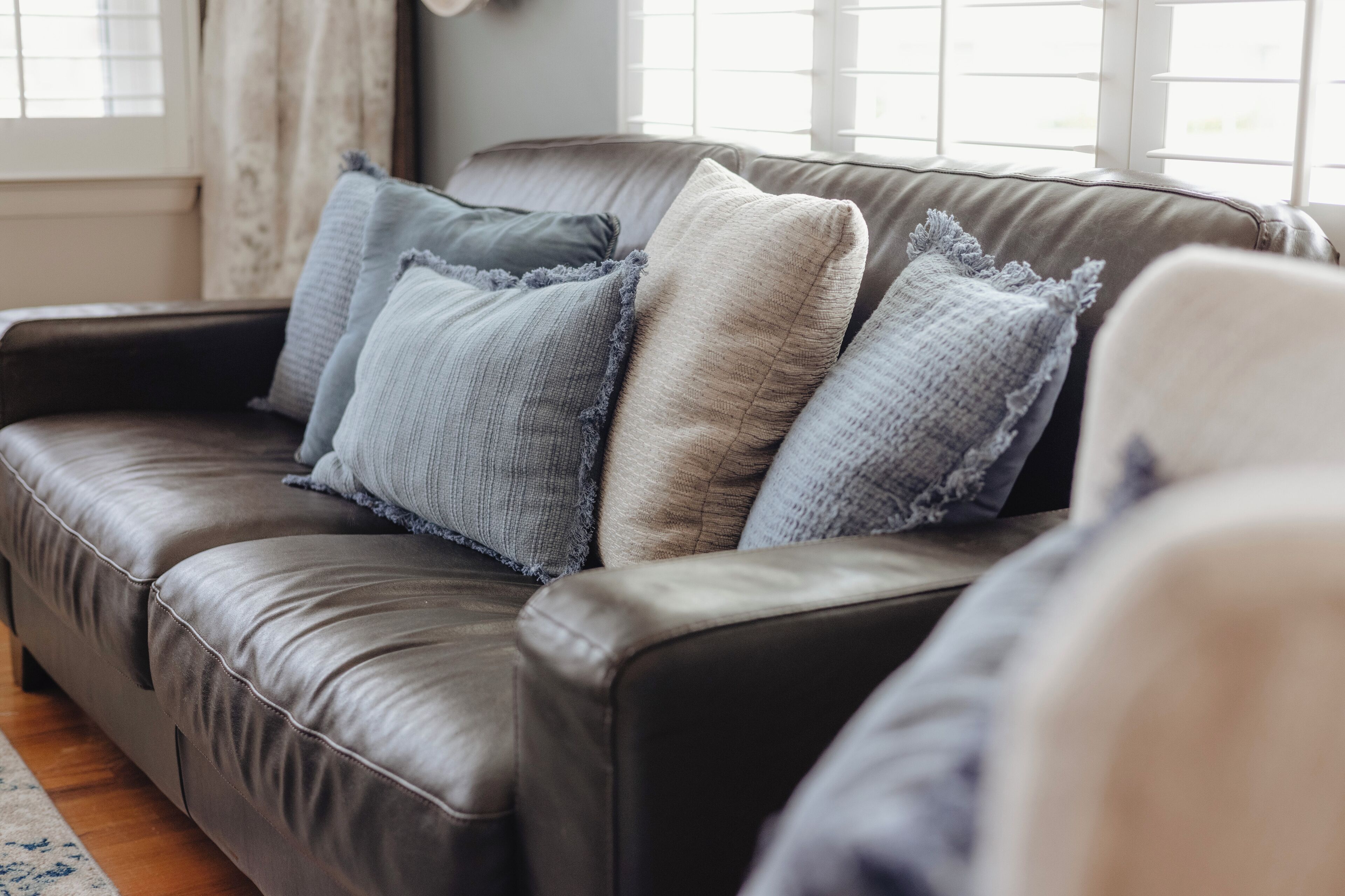 Un canapé en cuir marron agrémenté de plusieurs coussins dans différentes nuances de gris et de beige.
