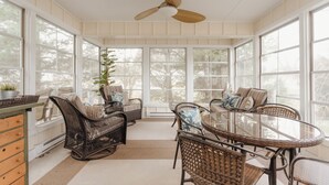 A sunroom with wicker furniture, a glass table, and a ceiling fan.