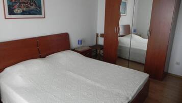 Quarto com uma cama grande, um guarda-roupa de madeira, uma cadeira e uma mesinha.