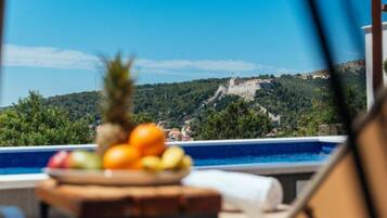A poolside view with a fruit bowl and a view of a historic hilltop fortress.
