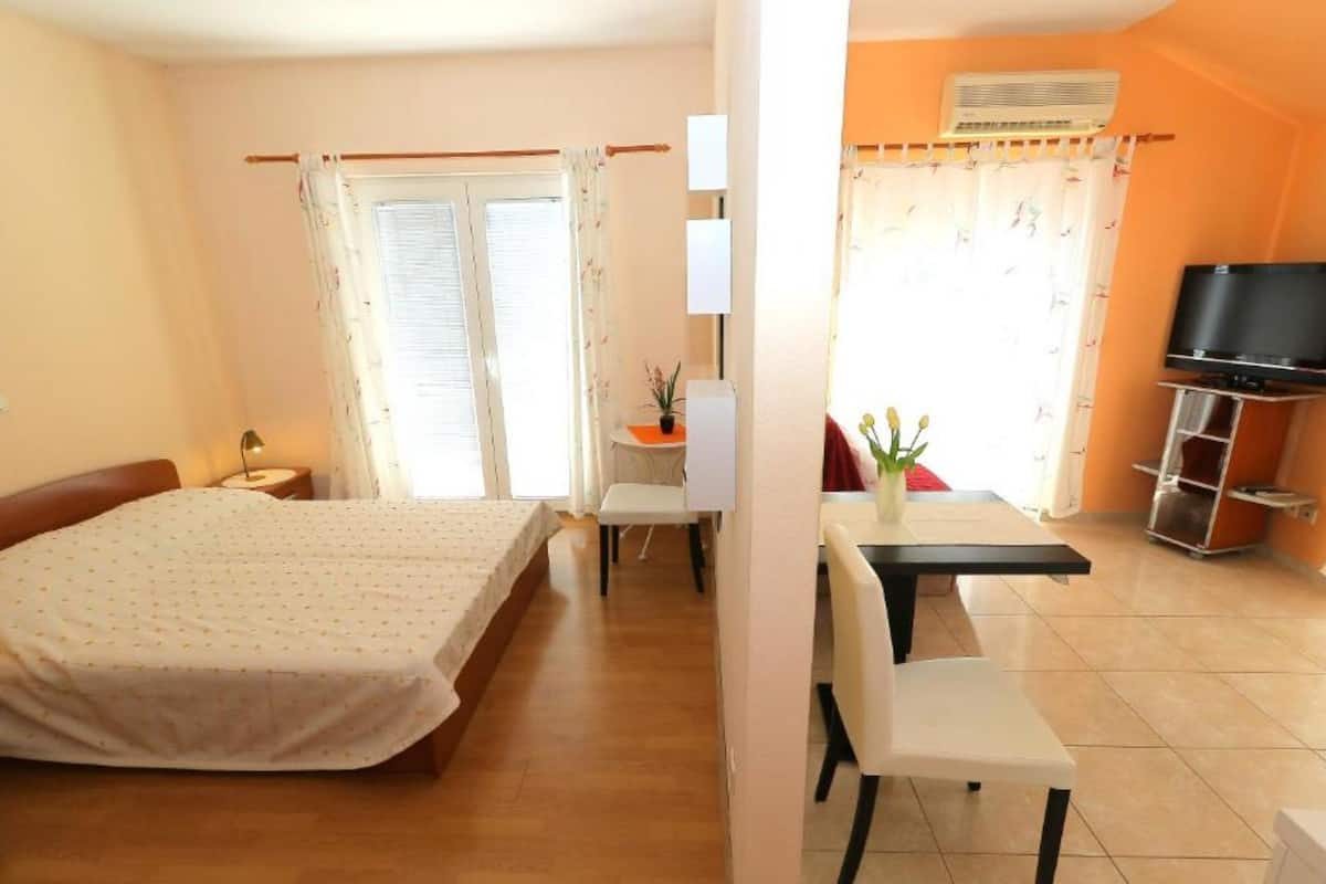 A hotel room with a bed, a desk, a chair, a television, and an air conditioning unit.