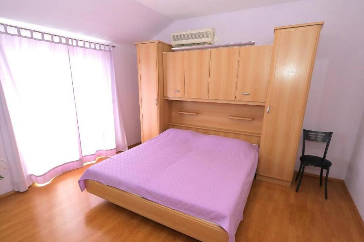 A bedroom with a wooden bed, a wardrobe, a chair, and a window with curtains.