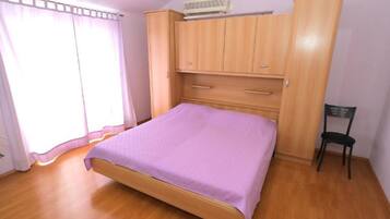 Un dormitorio con cama de madera, armario, silla y ventana con cortinas.