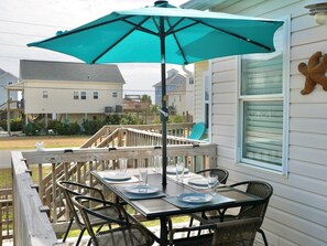 Une terrasse en bois avec une table dressée pour quatre personnes, un parasol et une vue sur les maisons au loin.