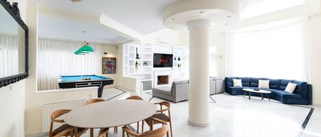 Amplia sala de estar con mesa de billar, un conjunto de sofás azules y una televisión.