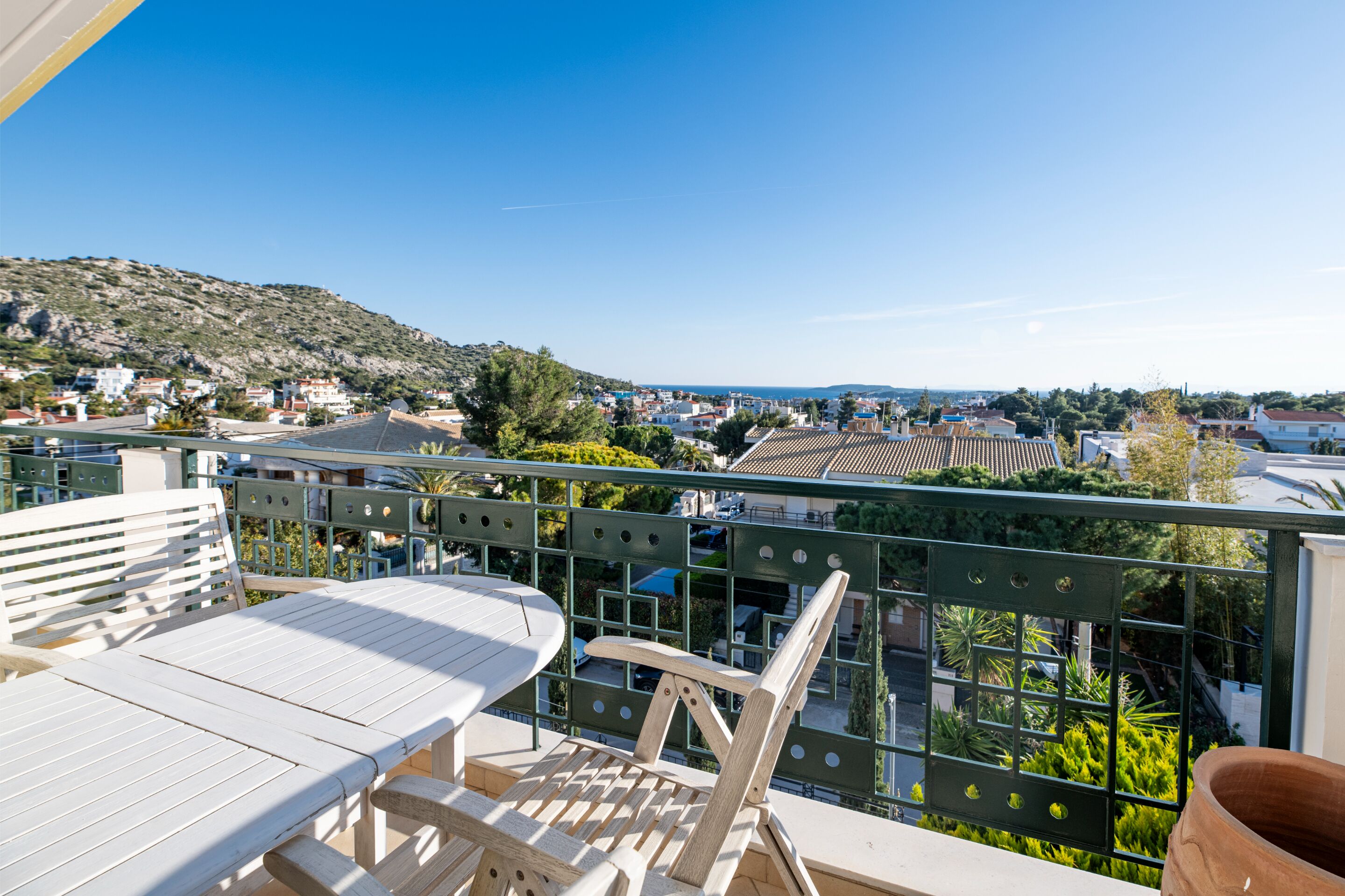 A balcony with a table and chairs, overlooking a town with buildings and a hill in the background.