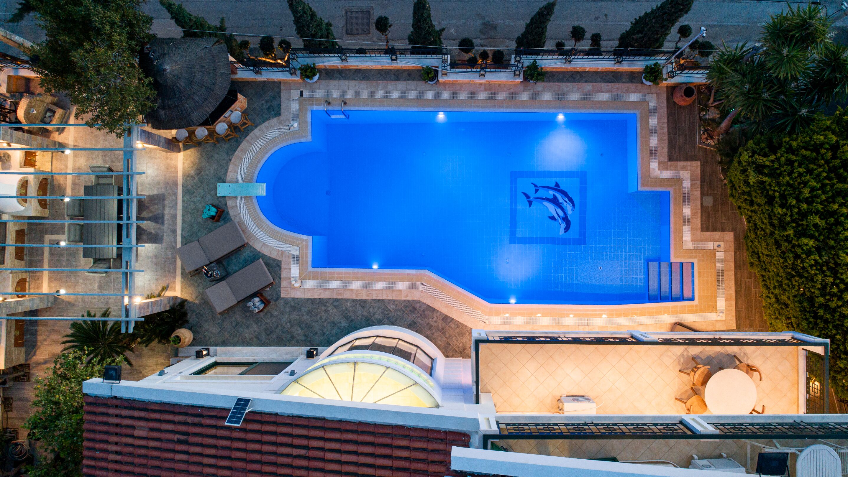 An aerial view of a hotel with a large swimming pool, sun loungers, and a covered seating area.