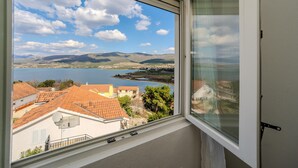 Une vue depuis une fenêtre donnant sur un lac, avec des bâtiments et des collines à l’horizon.