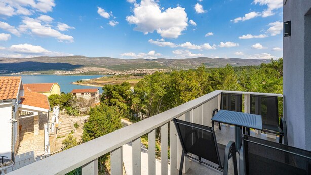 Un balcon offrant une vue sur une ville côtière, une étendue d’eau et des collines lointaines.