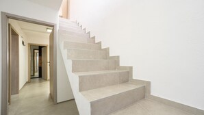 Un escalier moderne avec des marches de couleur beige et une rampe, menant à un couloir où se trouvent une porte et un interrupteur sur le mur.