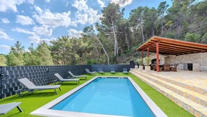 Une piscine rectangulaire avec une plage en pierre, entourée de gazon artificiel vert et de chaises longues grises.