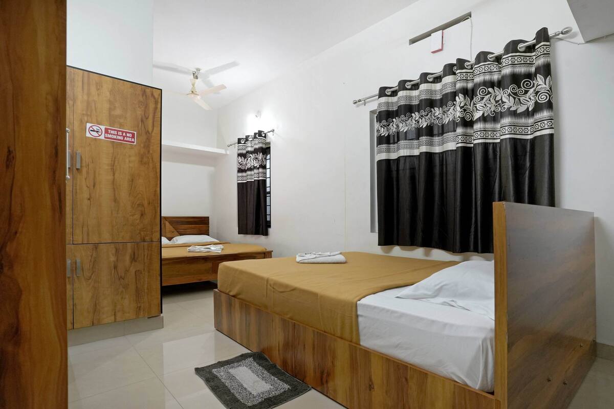 A bedroom with a wooden wardrobe, two single beds, a ceiling fan, and a no-smoking sign.