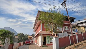 A two-story building with a red and white facade, a visible entrance, and a sign indicating it is a hotel. - Hillside Hideaway (Gudalur)