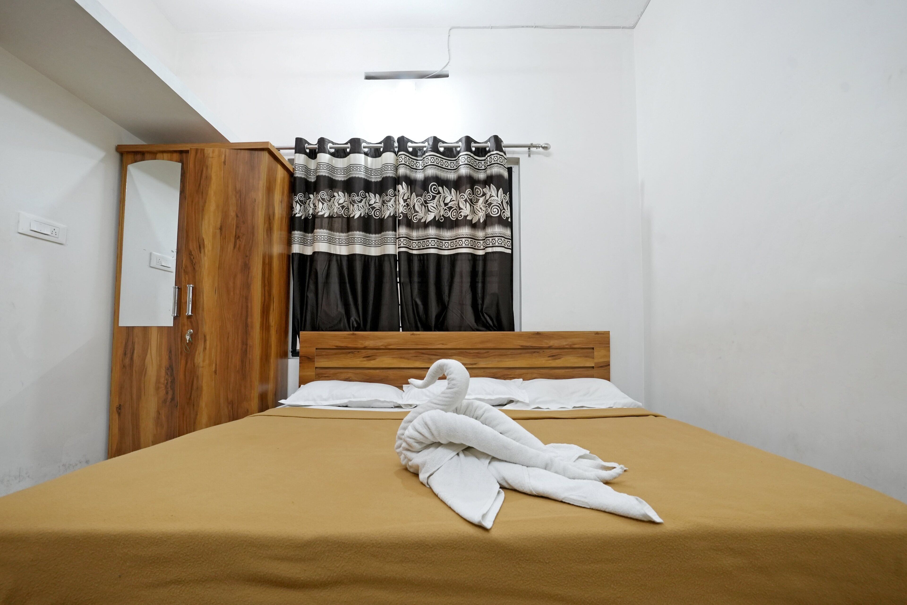 A neatly made bed with a brown bedspread, a wooden headboard, and a decorative curtain.
