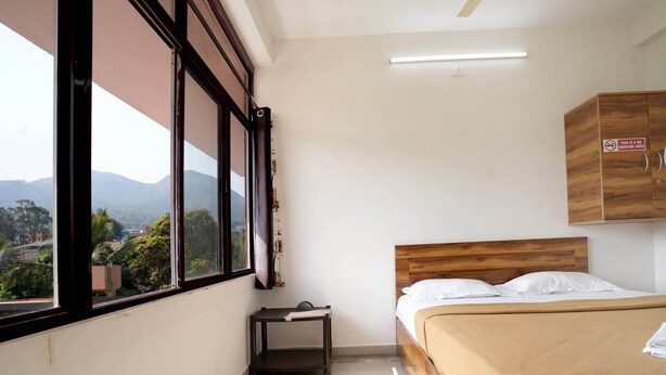 A bedroom with a bed, a nightstand, a window with a view of mountains, and a sign indicating a no-smoking area. - Hillside Hideaway (Gudalur)