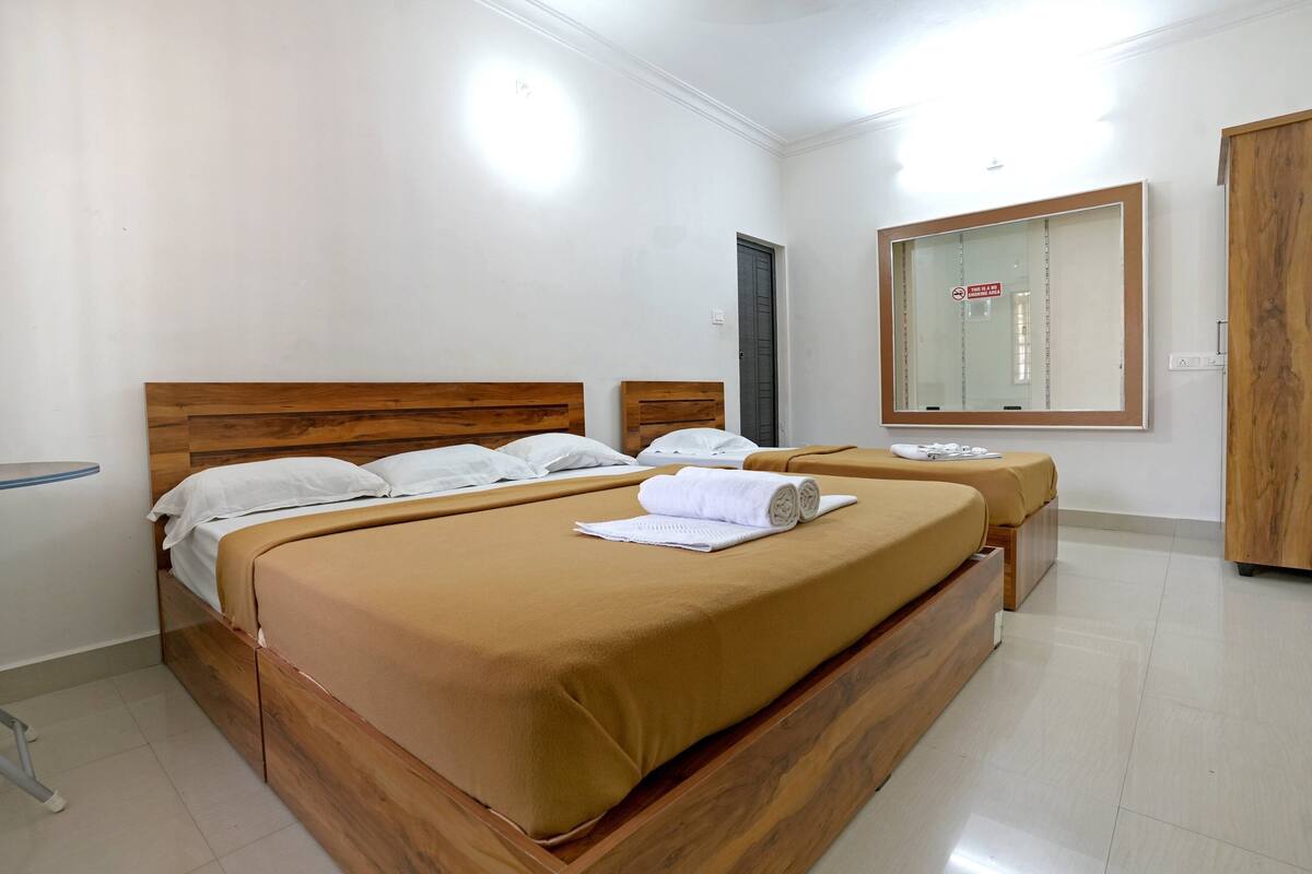 A hotel room with two wooden beds, white bedding, a wooden wardrobe, and a large mirror on the wall.