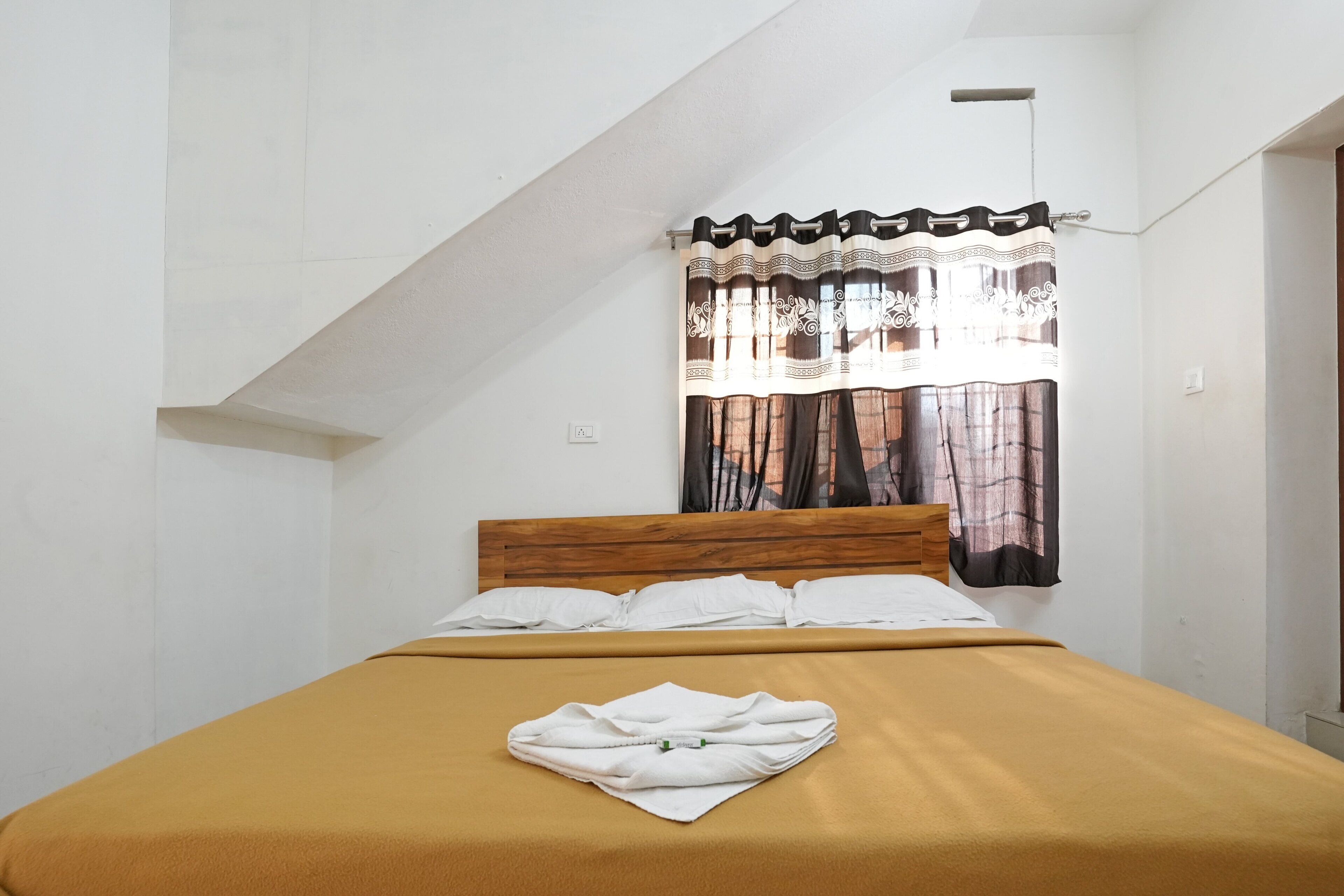 A single bed with a wooden headboard, a brown bedspread, and a folded white towel on the bed.