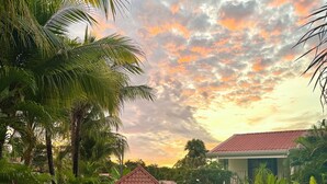 A swimming pool surrounded by lush greenery and a small building with a red roof. - Pura Armonia Condo with Outdoor Patio (Playas Del Coco)