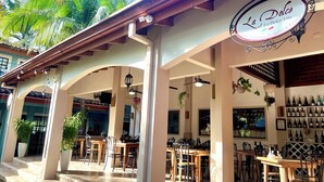 An outdoor café area with tables and chairs, a sign for 'La Dolce Vita International Restaurant & Pizzeria', and a wine display. - Pura Armonia Condo with Outdoor Patio (Playas Del Coco)