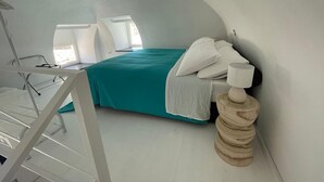 A modern bedroom with a curved ceiling, a bed with teal bedding, white pillows, and a wooden sculpture.