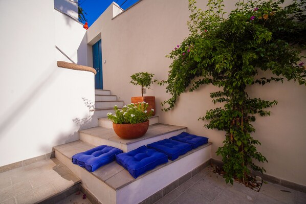 Un ensemble de marches extérieures agrémentées de coussins bleus, un pot de fleurs et une plante grimpante devant un mur blanc.