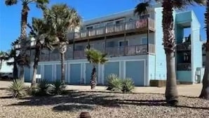 Een hotel met meerdere verdiepingen en balkons, omringd door palmbomen en een helderblauwe lucht.