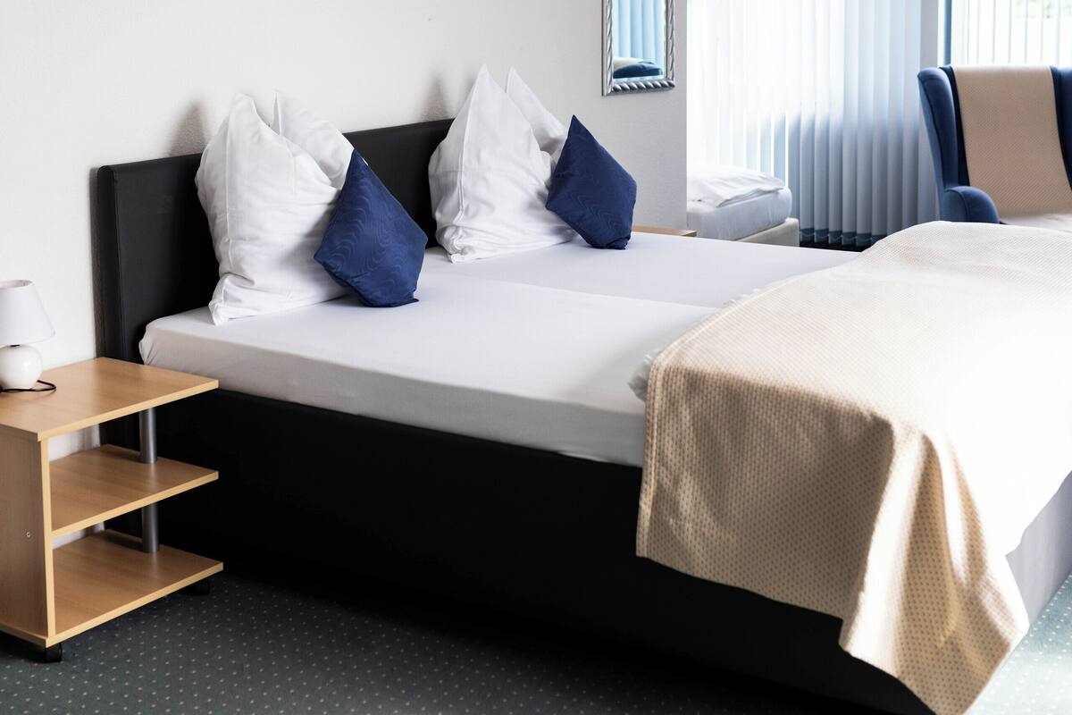 Ein Hotelzimmer mit Bett, Nachttisch, Spiegel und einem fensterbepflanzten Fenster.