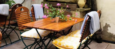 Un patio al aire libre con una mesa y sillas de madera, rodeado de follaje y un muro de piedra.