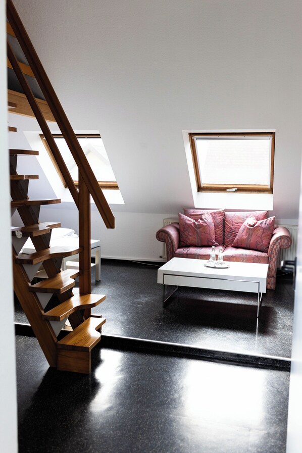 Una sala de estar moderna con una escalera de madera, un sofá rosa, una mesa de centro blanca y un tragaluz.