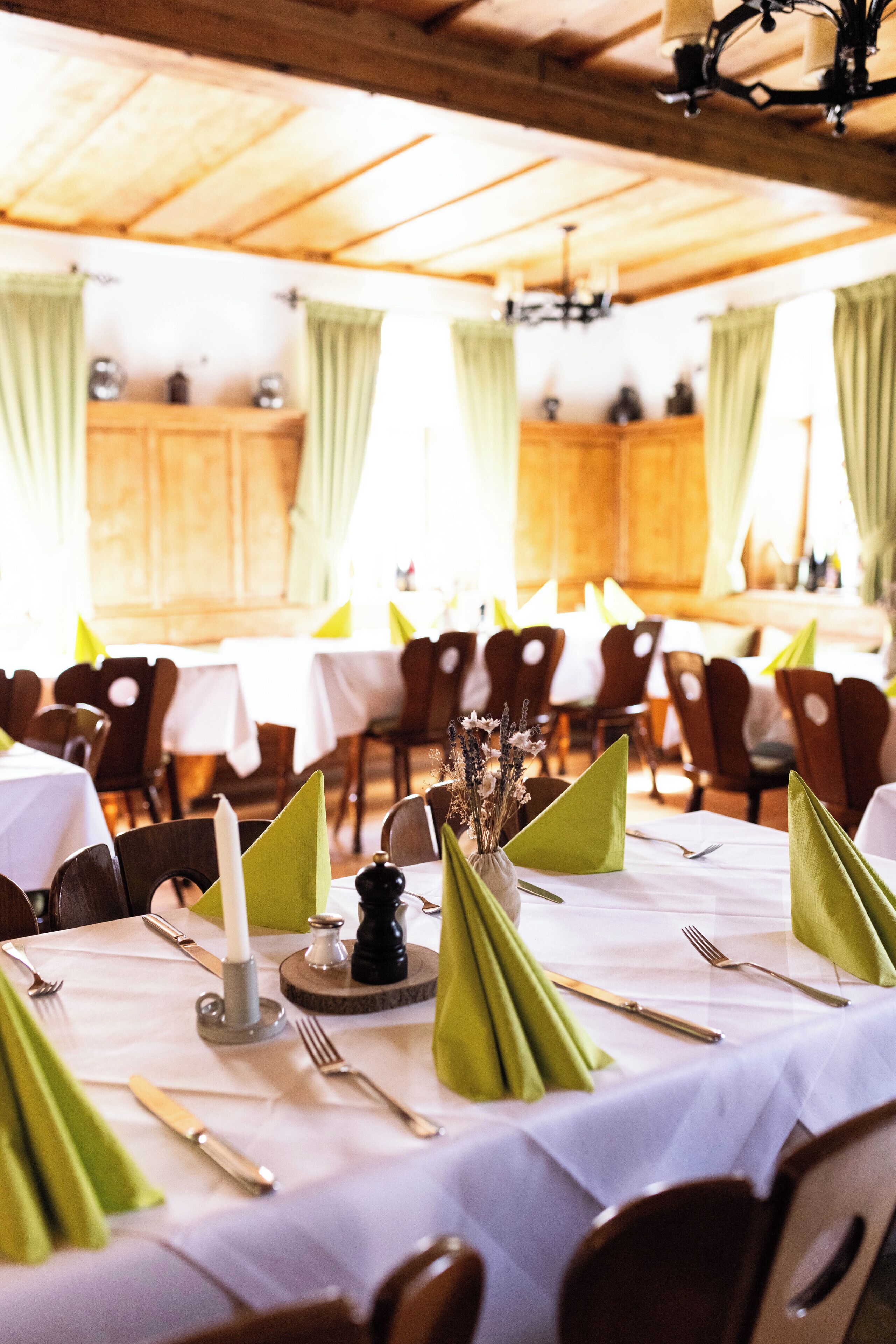 Un espace repas avec des tables dressées pour le service, un plafond en bois et des rideaux verts.