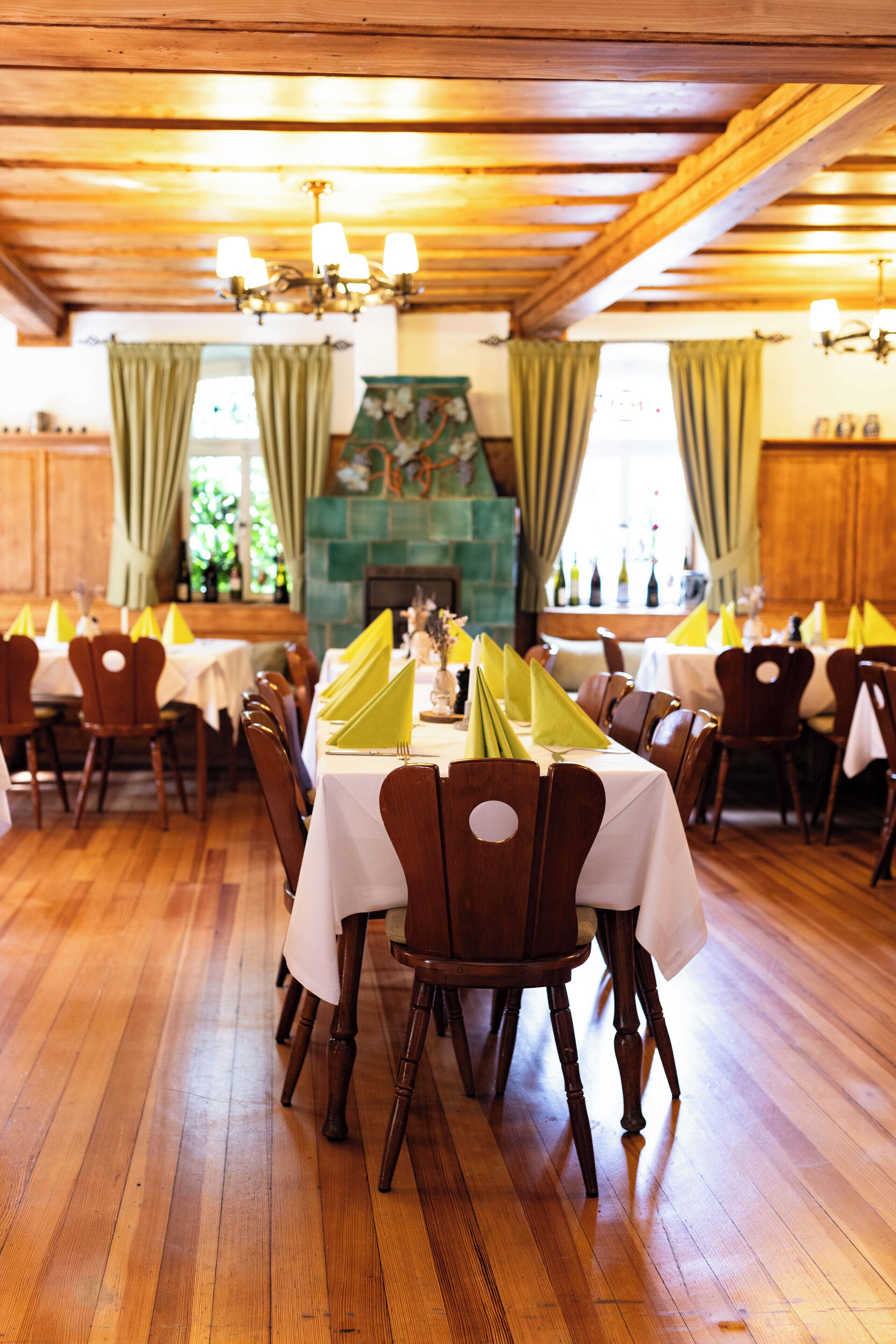 A dining area with wooden floors, tables set with white tablecloths and yellow napkins, and a fireplace in the background.
