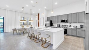 Una cocina moderna con una isla central, armarios grises, electrodomésticos de acero inoxidable e iluminación colgante.