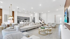 Una sala de estar moderna con un sofá, sillones, un comedor y una cocina al fondo.