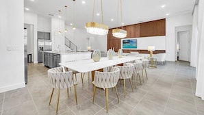Una cocina moderna con armarios blancos, un refrigerador de acero inoxidable y un comedor con una mesa y sillas blancas.