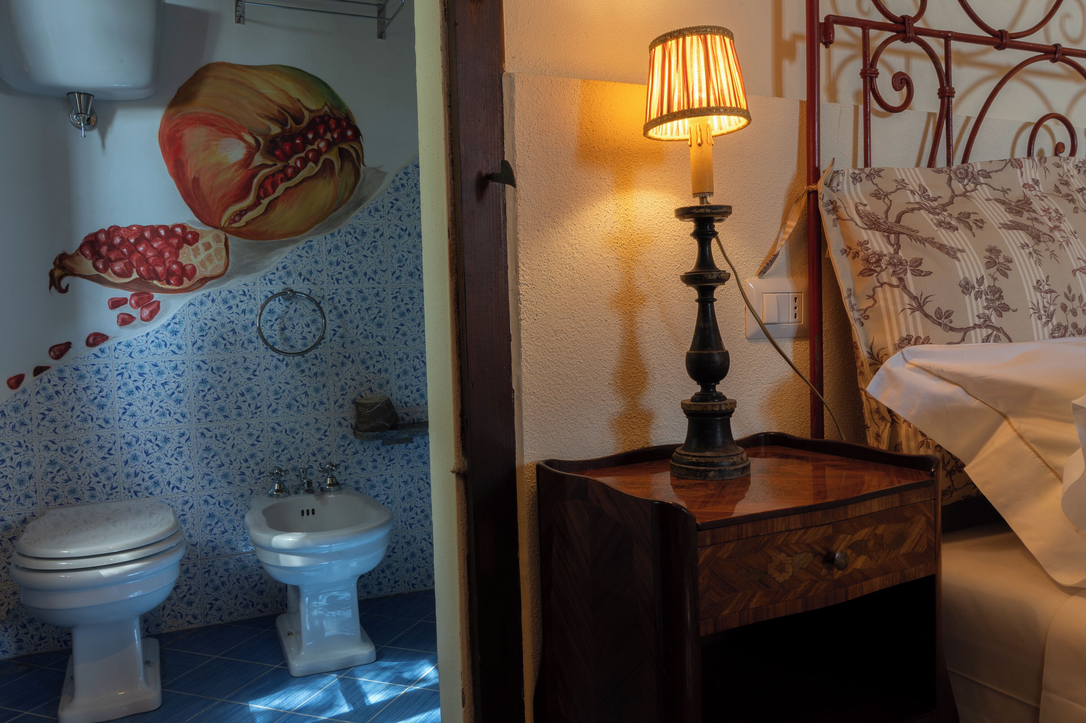 Casa de banho com sanita, bidé e um mural decorativo de romãs na parede.