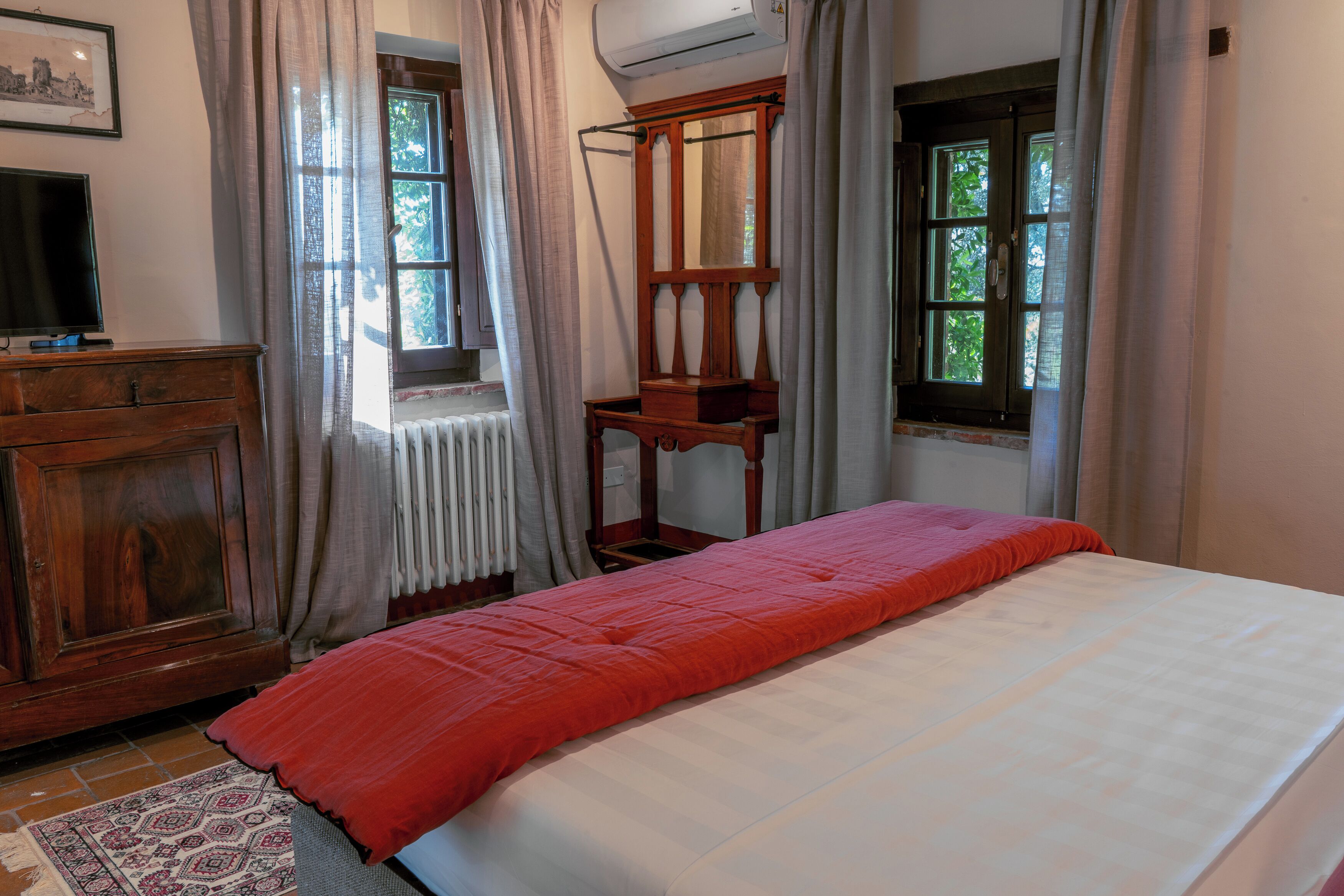 A room with a bed, a wooden dresser, a mirror, and two windows with curtains.