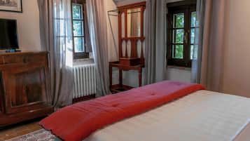 Une pièce comprenant un lit, une commode en bois, un miroir et deux fenêtres avec des rideaux.