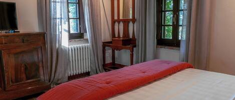 A room with a bed, a wooden dresser, a mirror, and two windows with curtains.