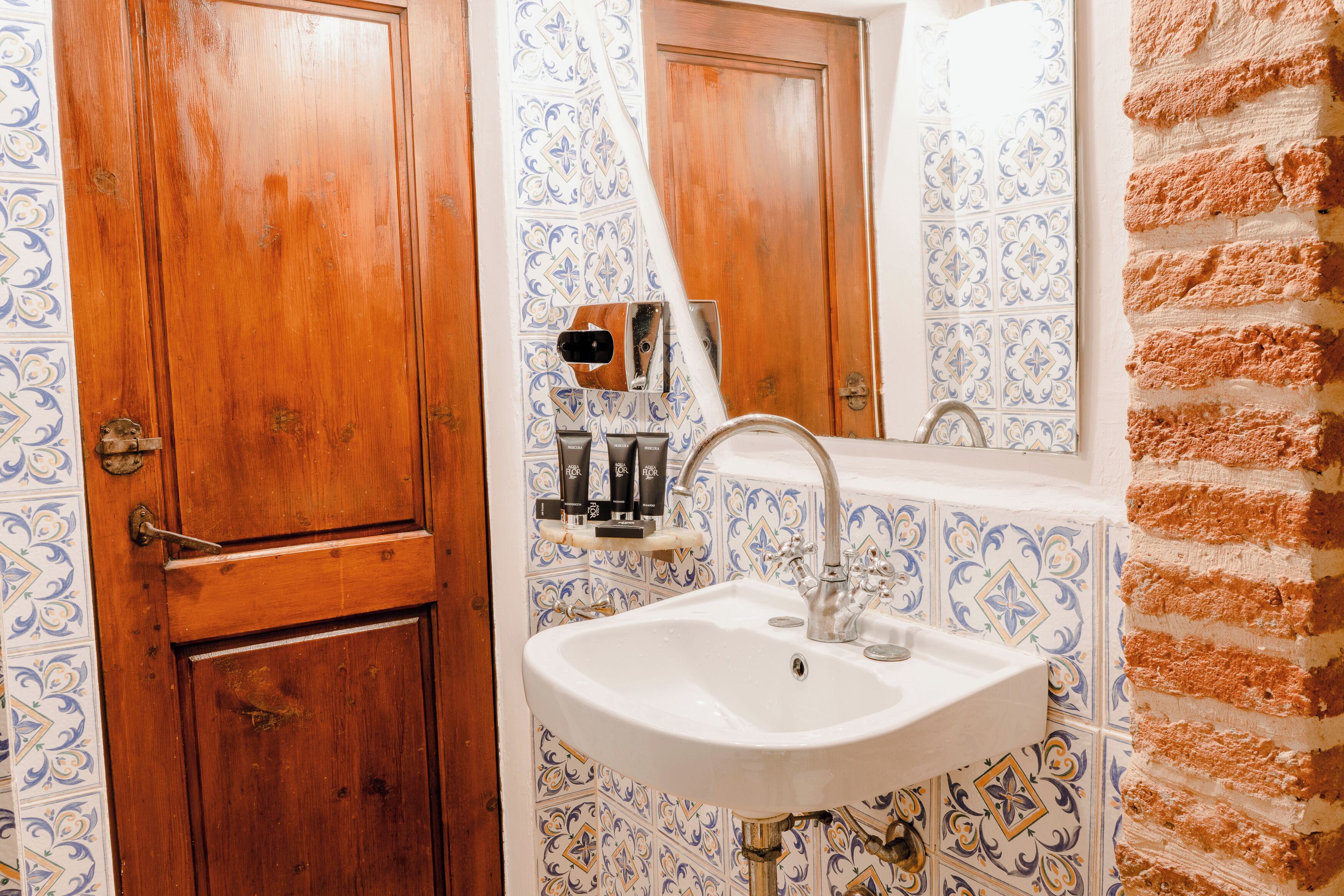 A bathroom with a wooden door, a sink with a mirror, and decorative blue and white tiles.