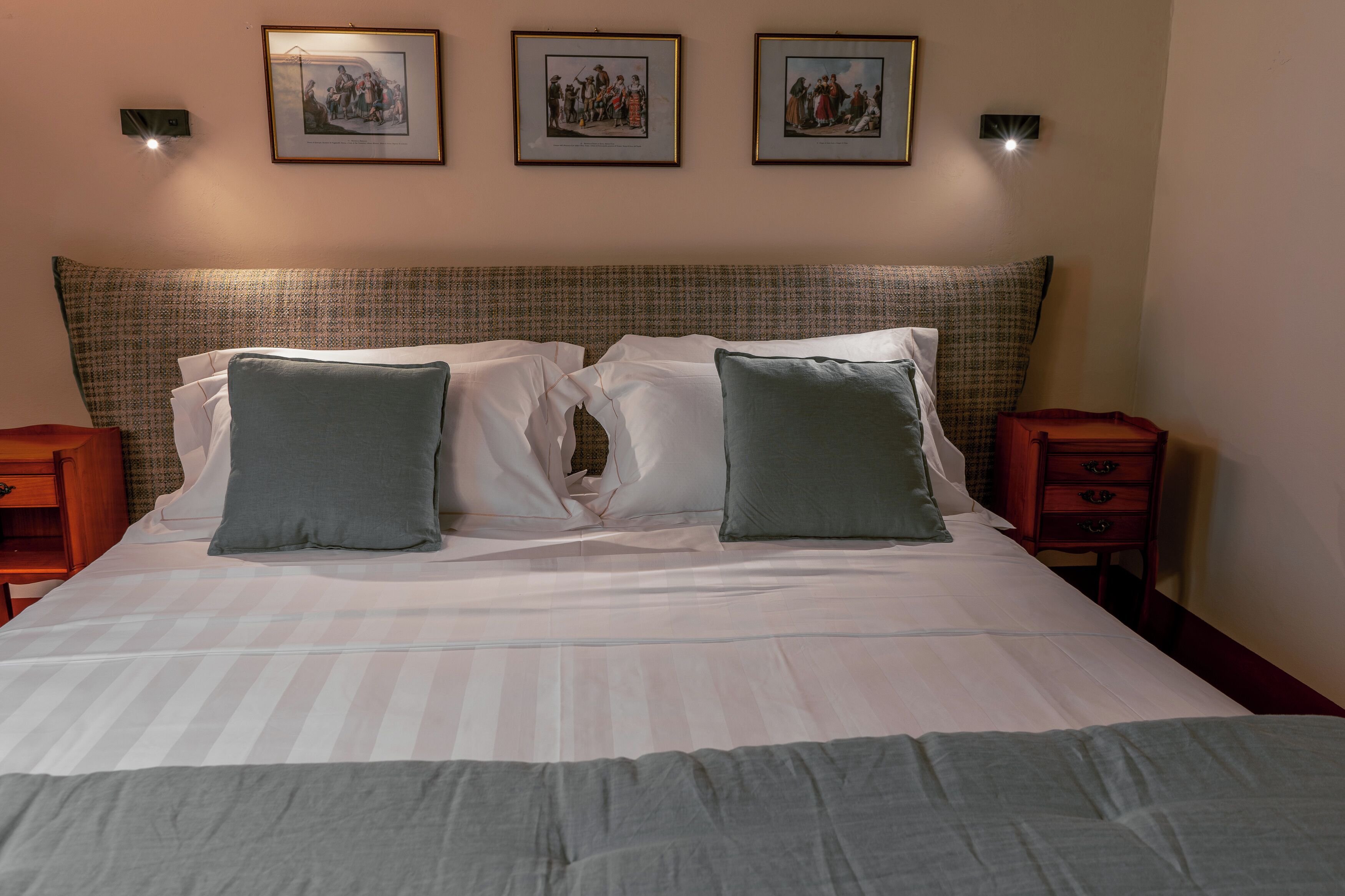 A neatly made bed with two pillows, a headboard with a patterned design, and three framed pictures on the wall.