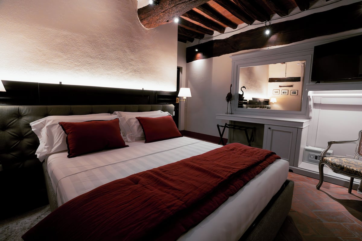 A bedroom with a large bed, a red blanket, and a wooden headboard.