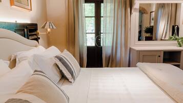 A hotel room with a large bed, a bedside table with a lamp, a mirror, and a view of the outdoors through a window.