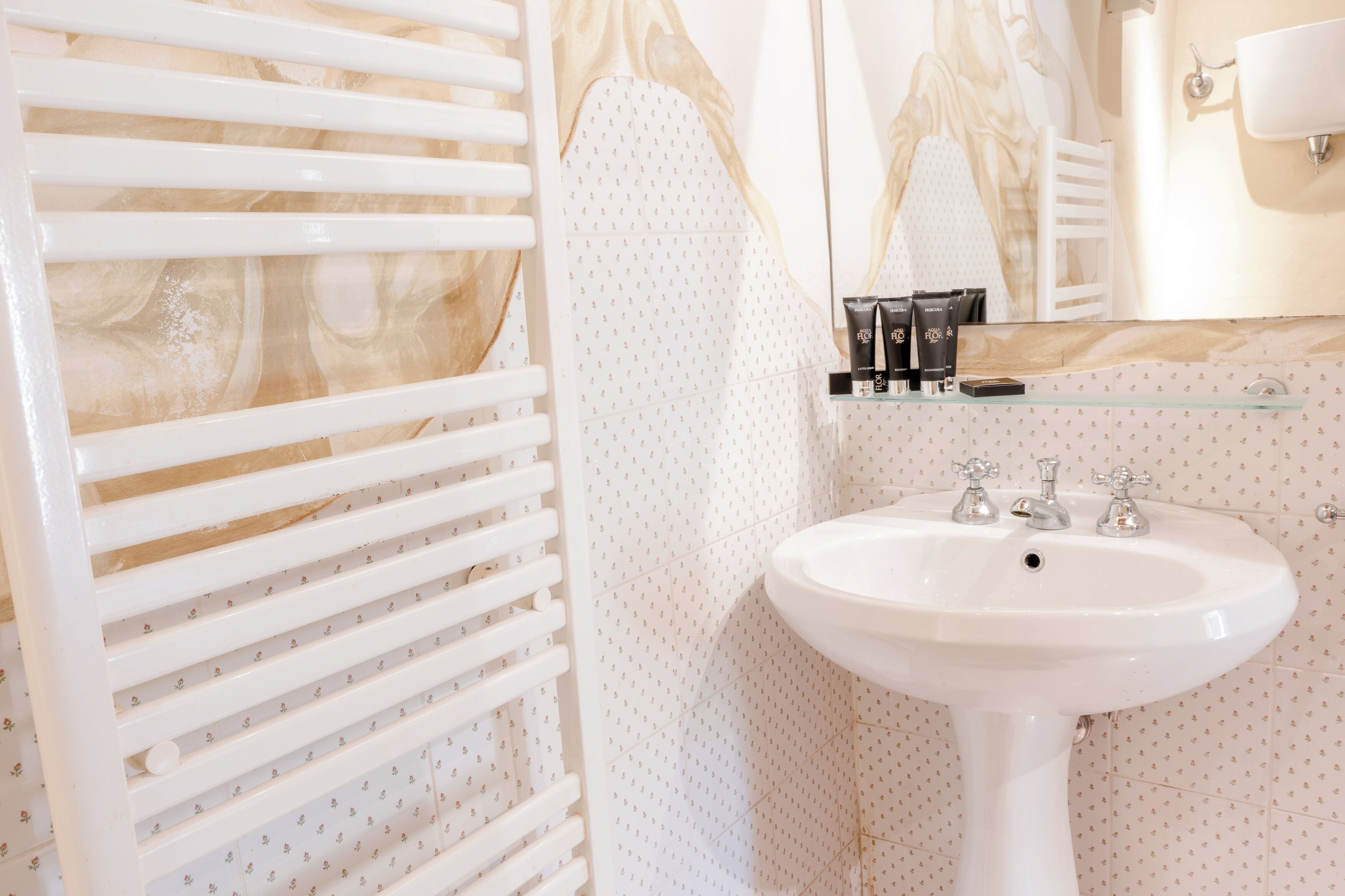 Un baño con lavamanos blanco, un estante de vidrio con artículos de aseo y un perchero para toallas.