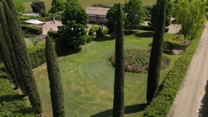 Un jardin bien entretenu, agrémenté de grands cyprès, d’une pelouse et d’un bâtiment dont le toit est recouvert de tuiles.